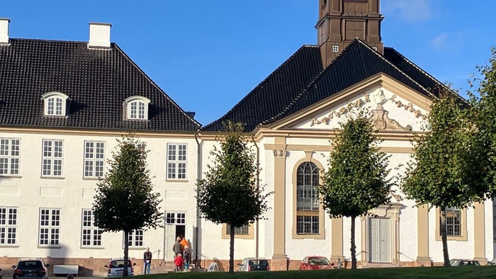 Stor, gul bygning med tårn og grønne træer foran