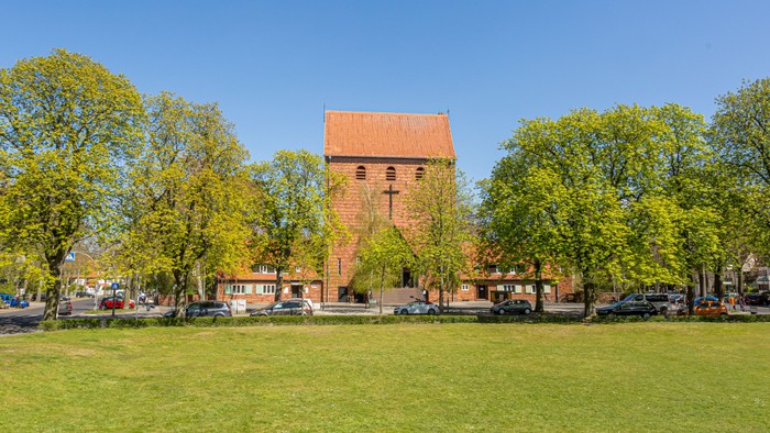 Ein roter Backsteinturm steht in einem grünen Park mit Bäumen und Gras.