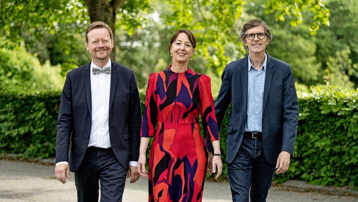 Tre professionelle personer står sammen i en park.