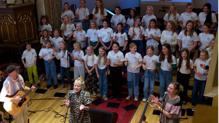 En gruppe børn og voksne optræder med sang og guitar på scenen