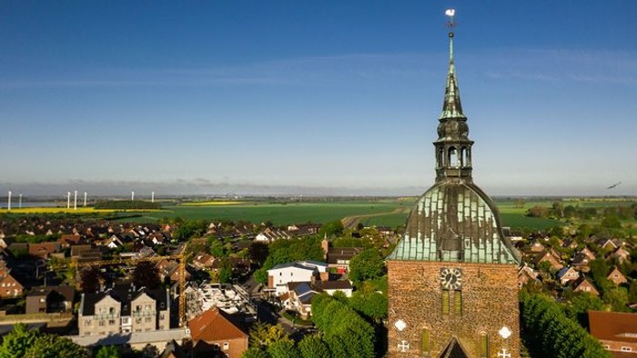 Ein Dorf mit einer Kirche und Windrädern im Hintergrund unter klarem Himmel
