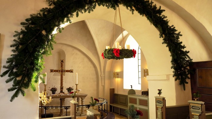 En indendørs kirke med juldekorationer, bl.a. en stor grønne kronede bog og røde roser.