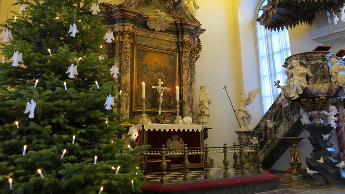 En juletree med lys og pynt til venstre for en præstestol med religiøse figurer.