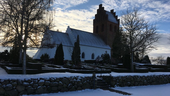En snedækket kirke med tårn og træer i forgrunden