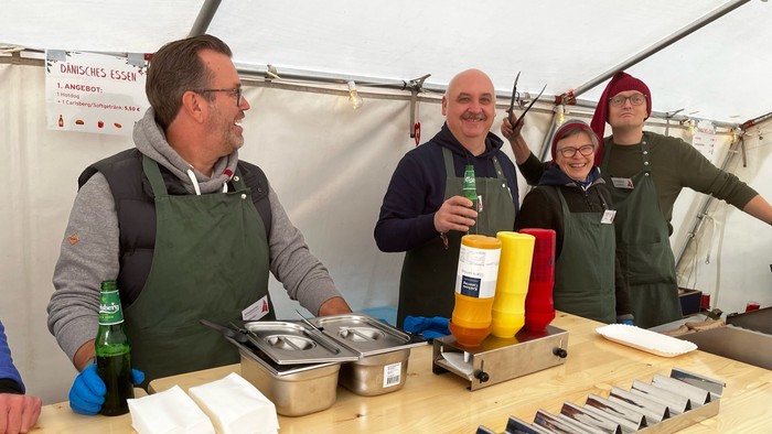 Fire mænd står bag en madstand og smiler.