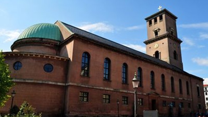 En rød murstenskirke med grøn kuppel og tårn.