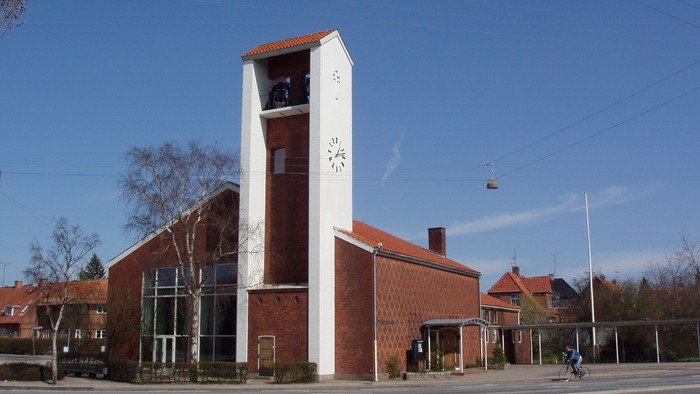 En rød murstenskirke med klokketårn og klokke.