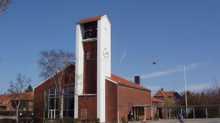 En rød murstenskirke med klokketårn og klokke.