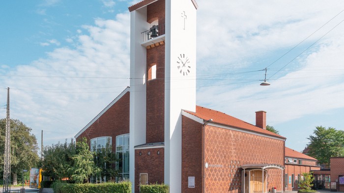 En rød murstenskirke med klokketårn og klokke.