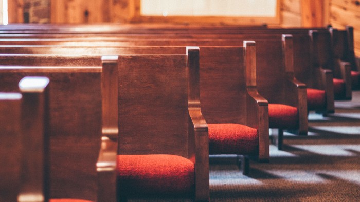 Wooden church pews with red cushions.