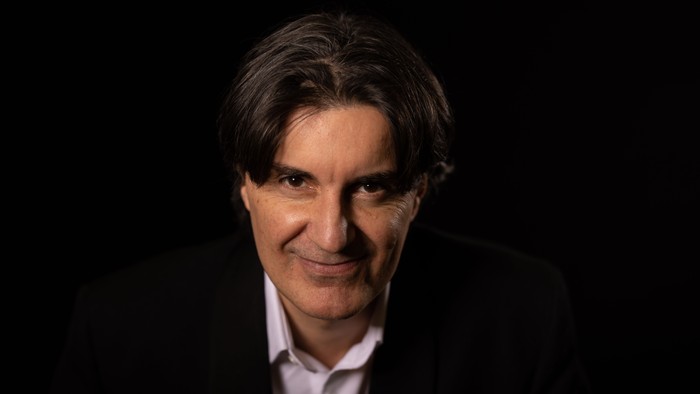 En mand med kort grå hår og mørke klæder, smilende mod kamera.