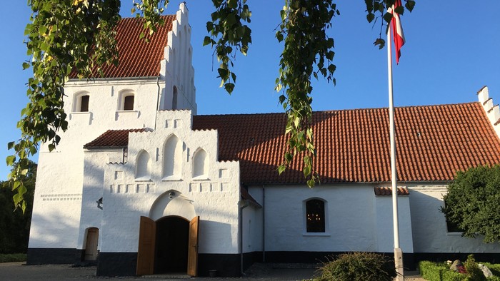 Hvid kirke med spiretårn og røde tag, med dansk flag på en stang foran