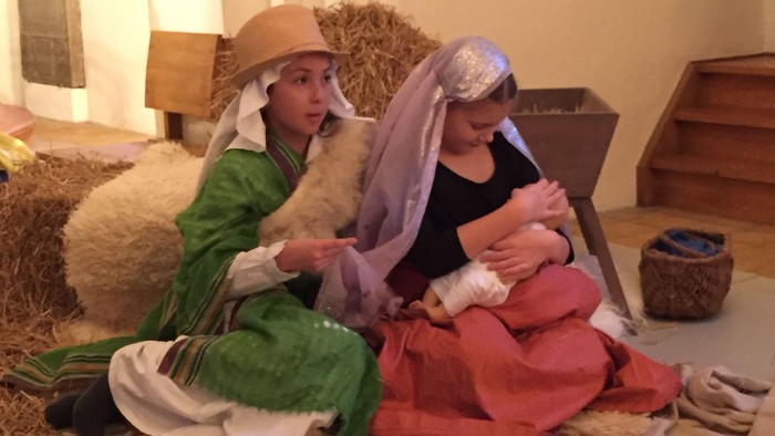 To børn i kostumer sidder på jorden med en puppe