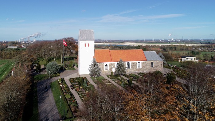 En lille kirke med klokketårn og rødt tag i landlig omgivelse