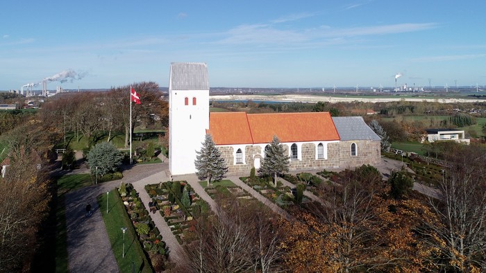 En lille kirke med klokketårn og rødt tag i landlig omgivelse