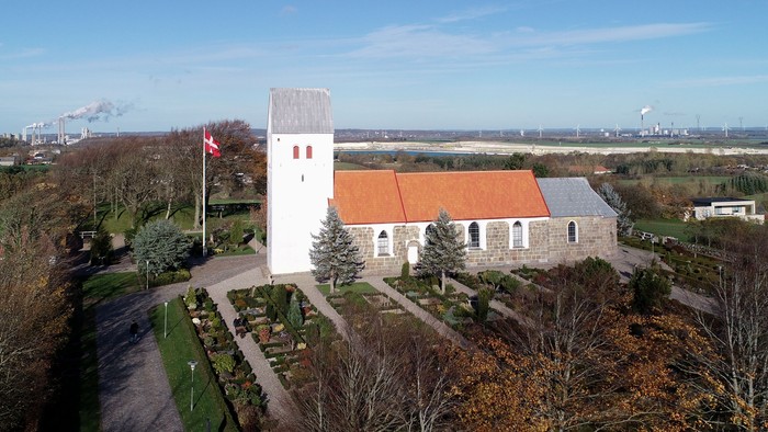 En lille kirke med klokketårn og rødt tag i landlig omgivelse