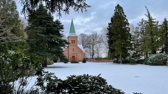 En lille kirke i snødekt landskab med træer.