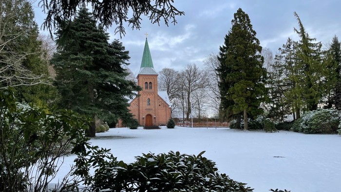 En lille kirke i snødekt landskab med træer.