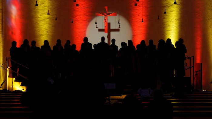 Gottesdienst in einer Kirche, viele Menschen sitzen vor einem beleuchteten Kreuz