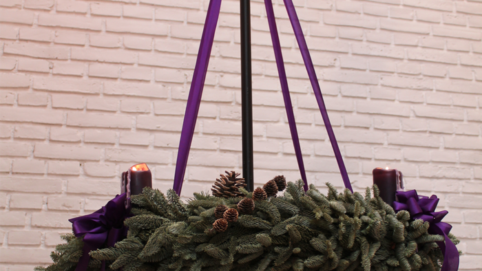 En hængende julekrans med lilla bånd og lys på en mur