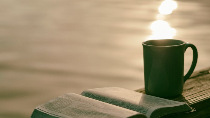Offenes Buch und Tasse auf hölzerner Oberfläche bei Sonnenuntergang