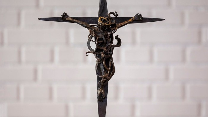 En smedejernskulptur af Jesus Kristus på korset står på en hvid flise.