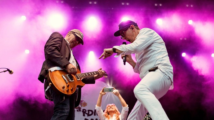 To bandmedlemmer på scene, en med guitar og en med mikrofon, under rød lys