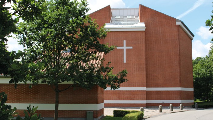 Et rødt murstenskirke med kors på fasaden og træ foran