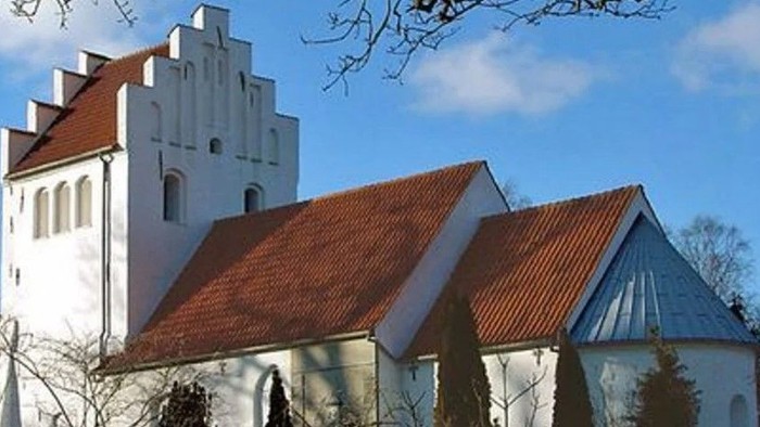 Et hvidt kirkebygningskompleks med røde tag og en tårn.