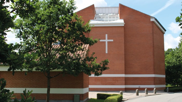 Et rødt murstenskirke med kors på fasaden og træ foran