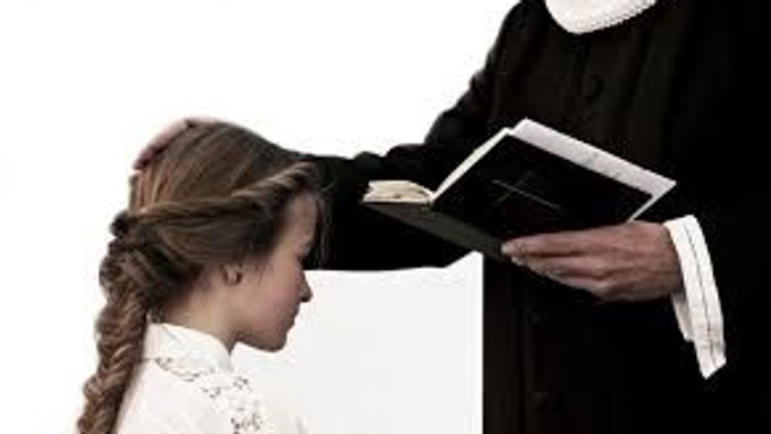 En ung pige modtager en bog fra en person i svart kapel.