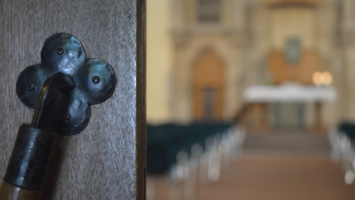Links ein altes Türschloss, rechts eine Kirchenbankreihe