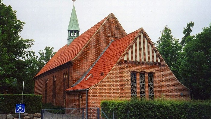 En rød murstenskirke med spiret og tag.