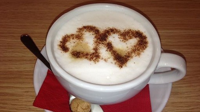 Eine Tasse Kaffee mit Herzchen aus Kakaopulver auf einem roten Untersetzer