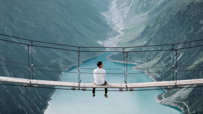 En person sidder alene på en bro over et vandfald i bjergene