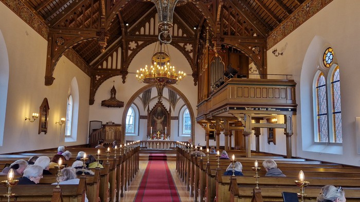Indre del af kirke med høje vægge, bænke og lysende kandle.