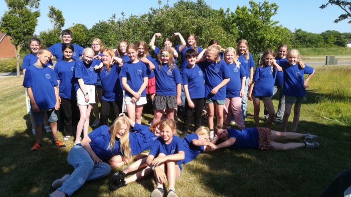 En gruppe unge i blå t-shirts samles på en eng.