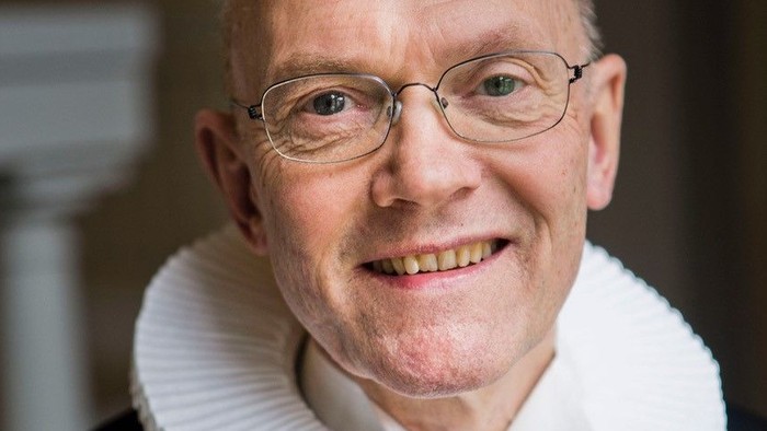 En smilende, eldre mand med glas og en hvid krage.