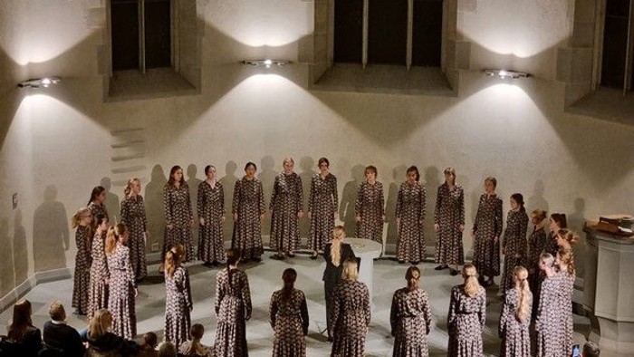 En gruppe kvinder i mønstrede kider står på scenen foran et publikum