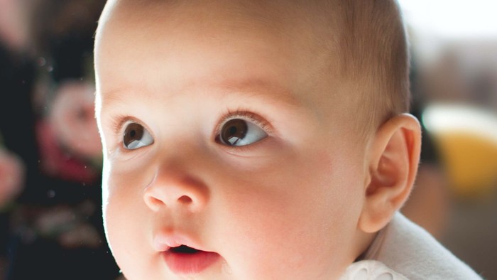Et spående lille barn med blå øjne og åben munn.