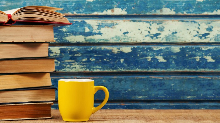 En stabel bøger og en gul tektaske på et blåt skab.