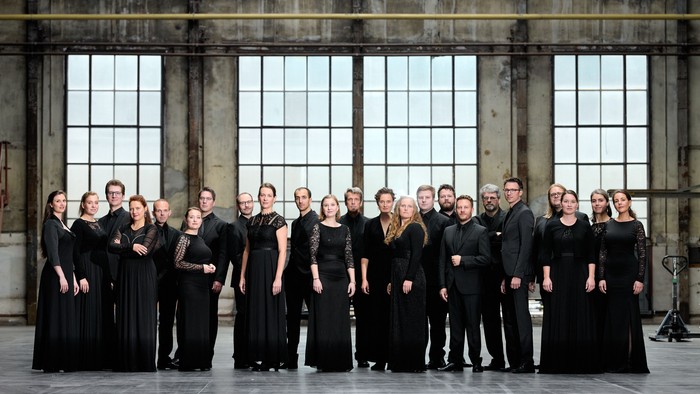 Ein Chor steht in einem großen, hellen Raum mit hohen Fenstern.