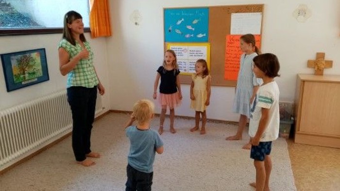 Eine Frau und fünf Kinder stehen in einem Raum mit bunten Pinnwänden.