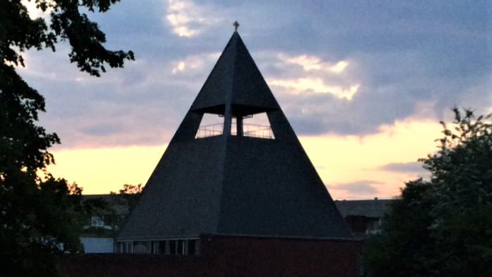 En pyramideformet kirke med tårn og en rød murvej til.