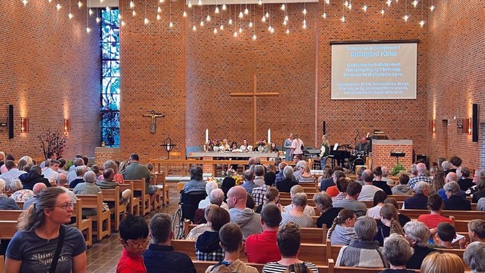 En stor kirke med mange tilstedeværende, lys og en prædikestol.