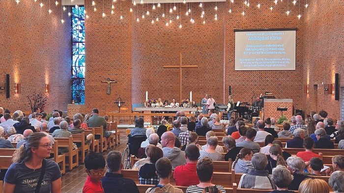 En stor kirke med mange tilstedeværende, lys og en prædikestol.