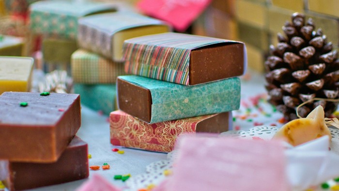 Colorful wrapped soaps and festive boxes arranged artistically with pinecone and confetti accents.