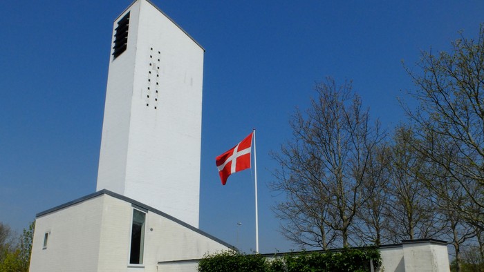 Hvid kirke med tårn og dansk flag på en klar dag