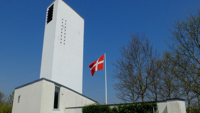 Hvid kirke med tårn og dansk flag på en klar dag