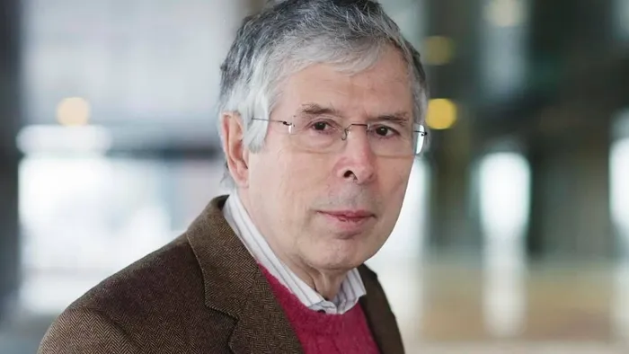 En mand i brune jakke og rød trøje står i et offentligt sted.